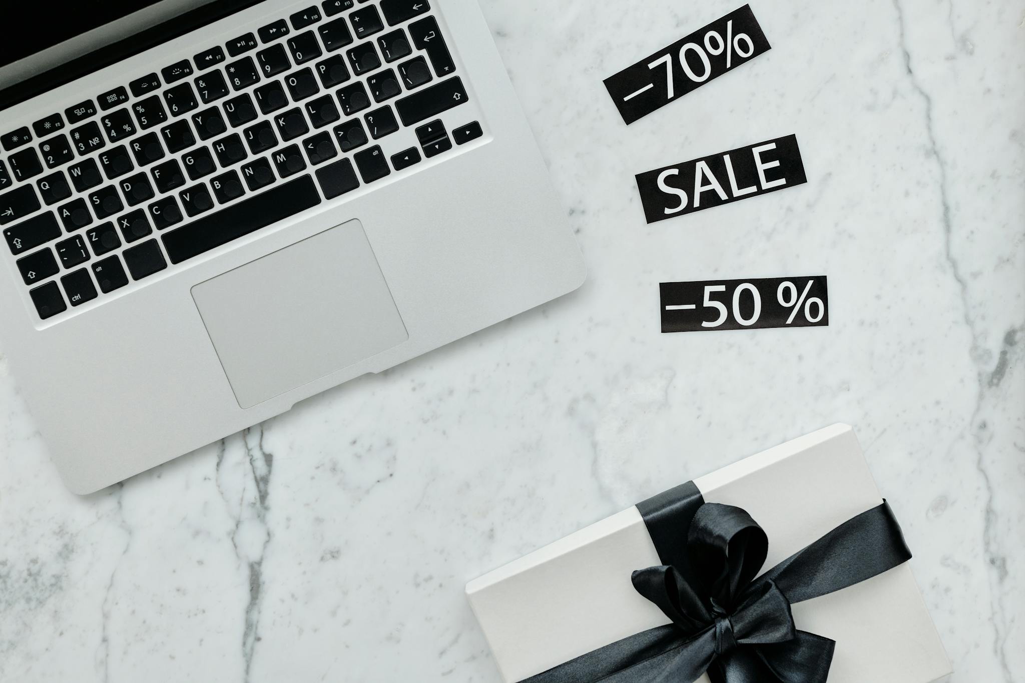 Marble workspace with a laptop, gift box, and sale tags offering discounts.